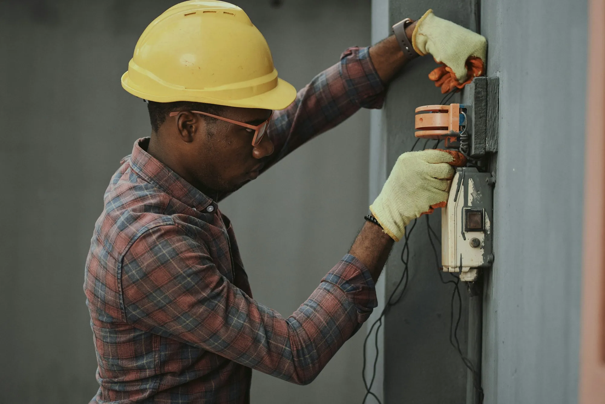 Technician in a hard hat working on a wall-mounted control box